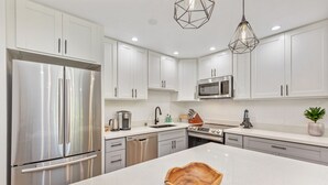 Een moderne keuken met witte kastjes, roestvrijstalen apparatuur, een centraal eiland en hanglampen.