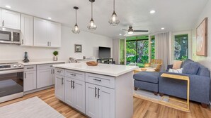 Een moderne keuken met witte kasten, een centraal eiland, hangende lampen en een zithoek met een blauwe bank en een houten bijzettafeltje.