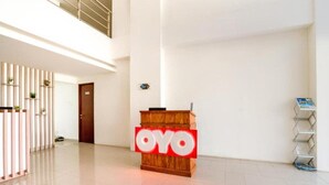 Een receptiegedeelte met een houten balie en een rood 'OYO'-bord, een betegelde vloer en een verticale plantenwand.