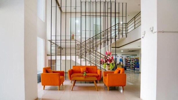 Een moderne lobby met een trap, oranje banken en een bloemstuk.