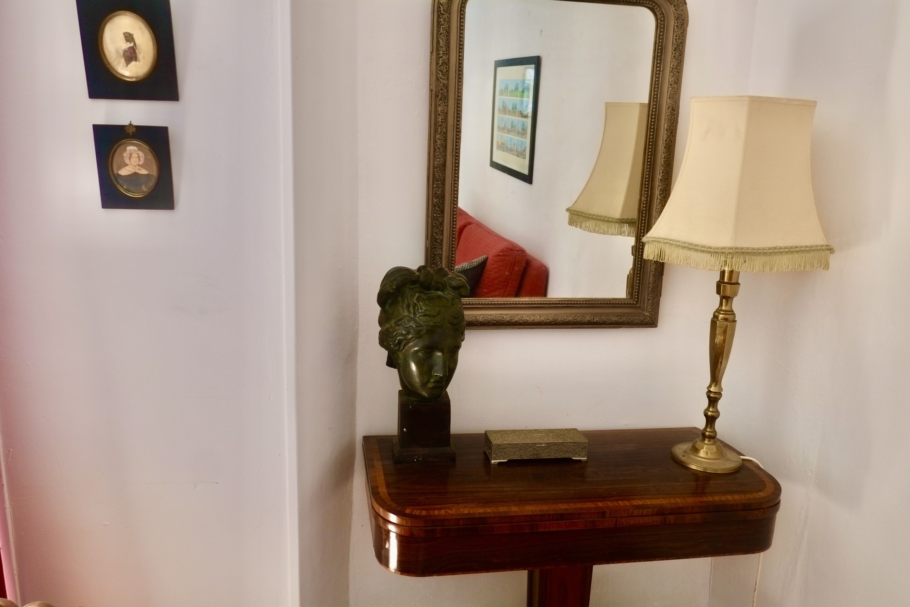 A wooden console table with a brass lamp, a framed mirror, and two framed pictures.