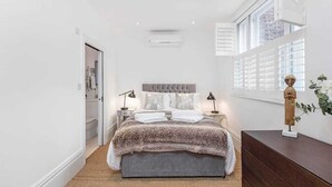 Ein Schlafzimmer mit einem großen Bett, Nachttischlampen, einem Schminktisch und einem Fenster mit Jalousien.