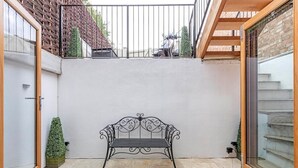 Ein Innenhof mit einer Metallbank, einem kleinen Topfpflanzen und einer Treppe, die in einen oberen Bereich führt.