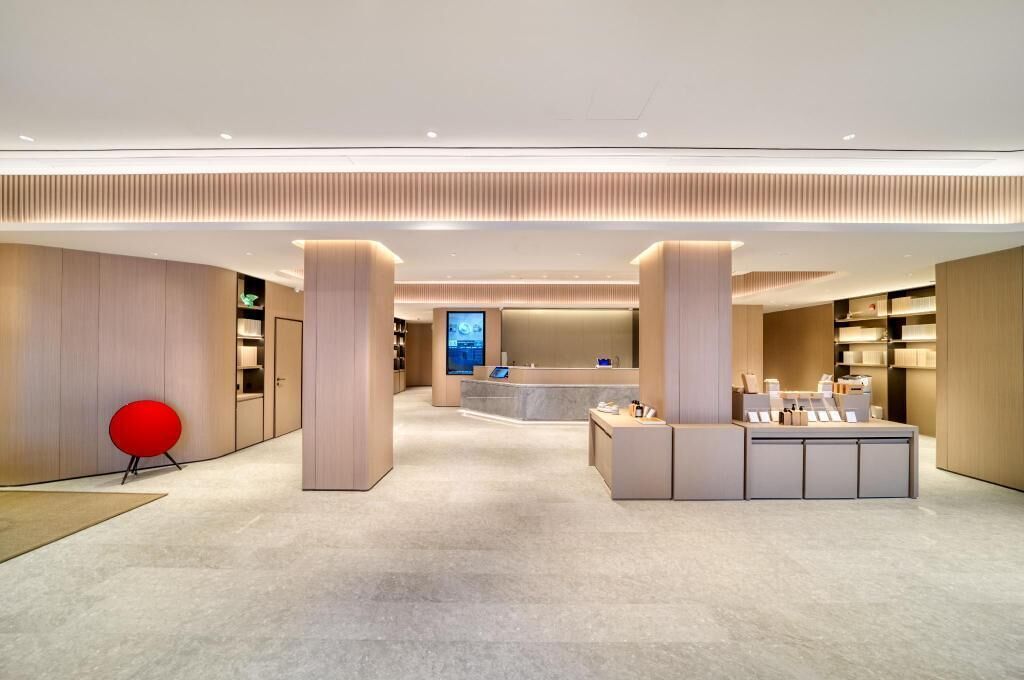 En modern hotellobby med en receptionsdisk, en röd stol och en stor skärm som visar information.