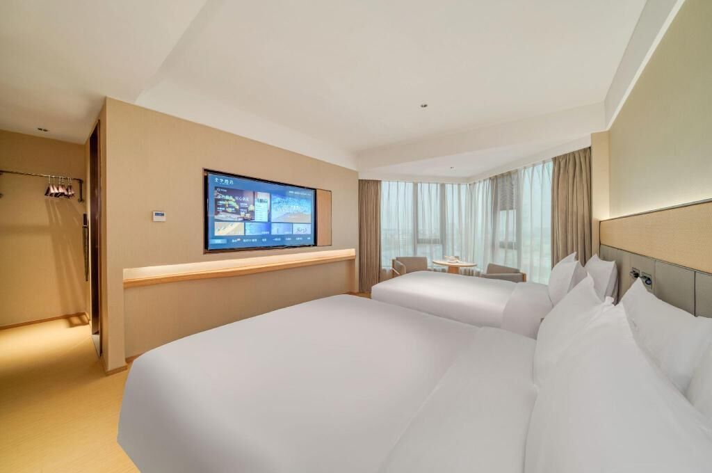 A hotel room with two beds, a TV mounted on the wall, a small table, and a chair.