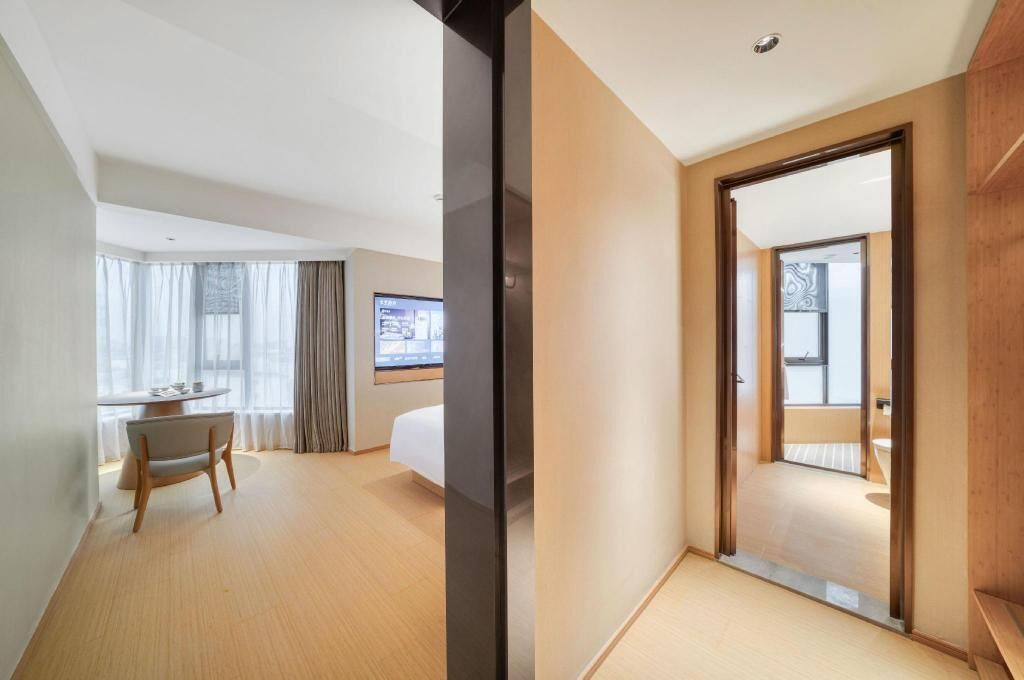 A hotel room with a bed, a desk, a chair, and a TV. There is a sliding door leading to a bathroom.