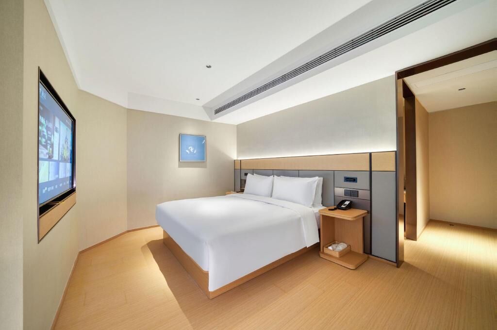 A modern hotel room with a large bed, a bedside table, a built-in TV, and a small bedside table with a phone.