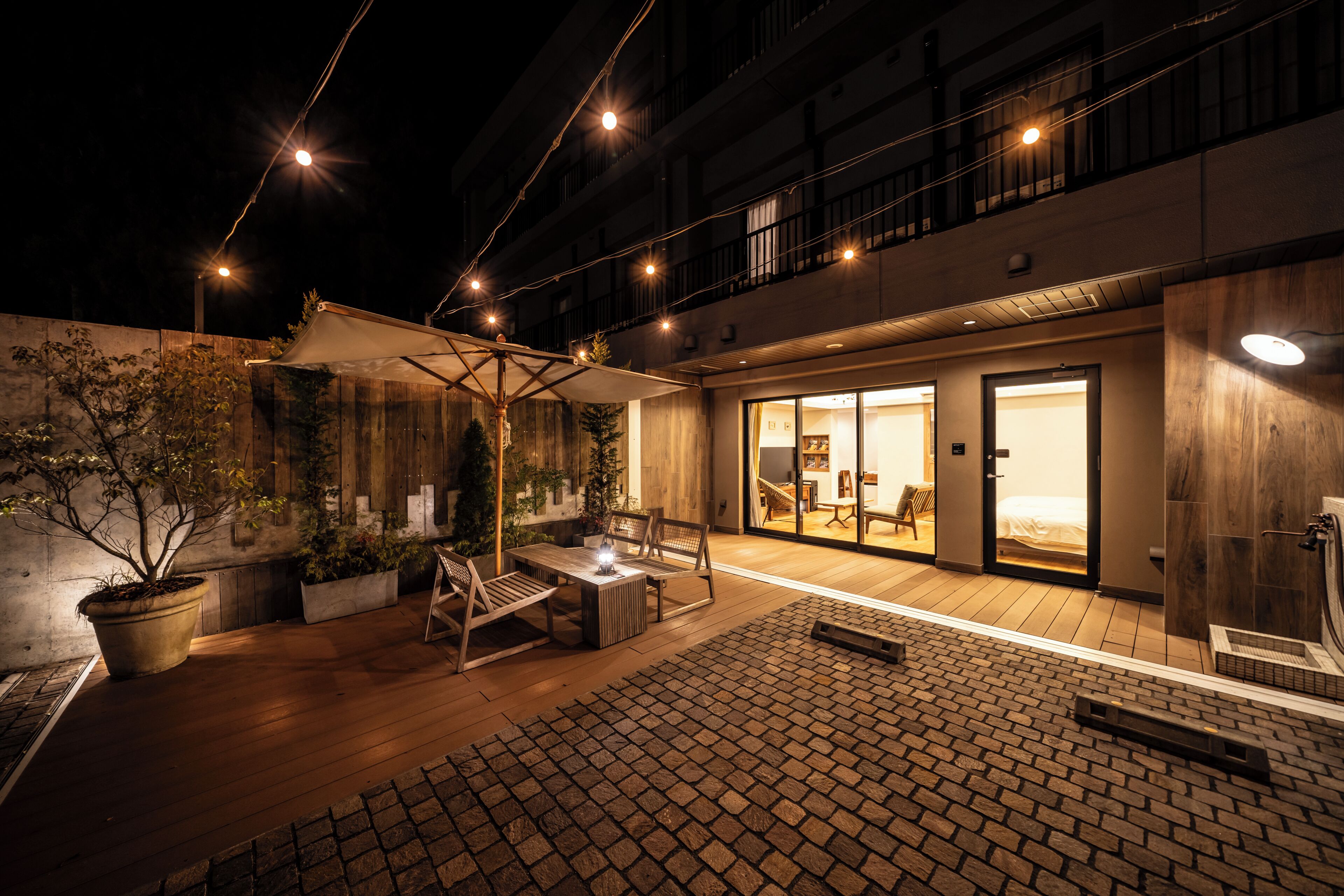Un espace extérieur aménagé en terrasse, avec un sol en bois, des plantes en pot et un coin salon abrité.