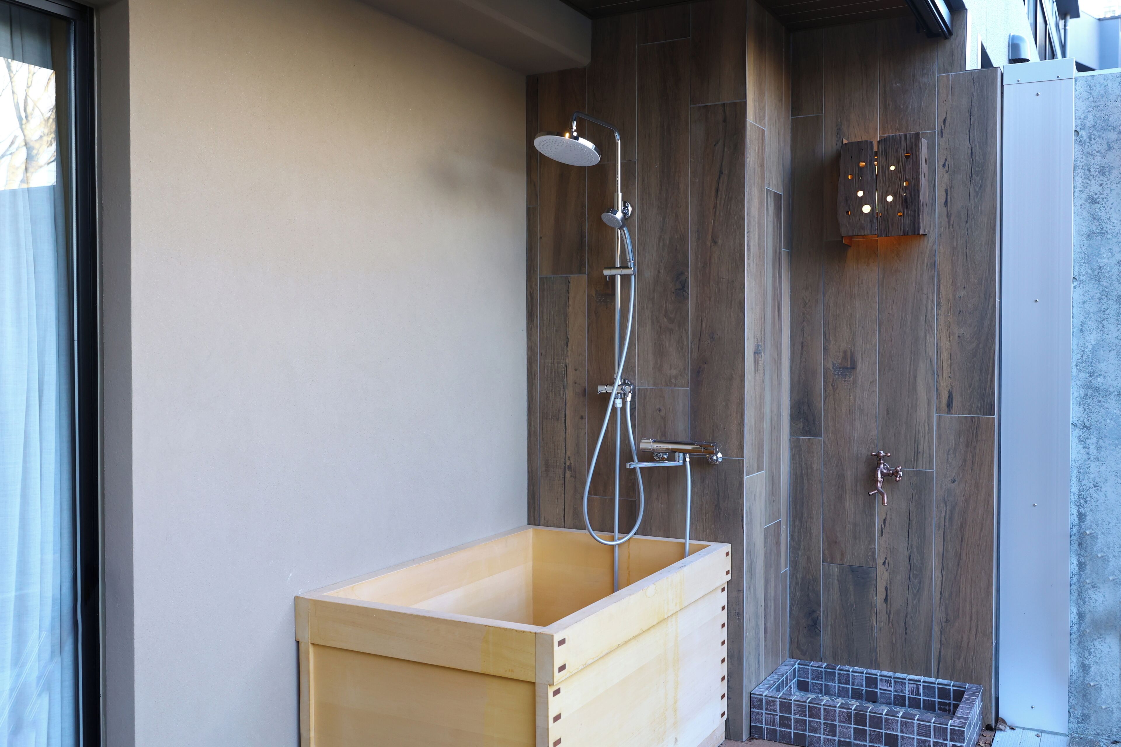Una bañera de madera con ducha, una puerta de madera con manija metálica y una pequeña cesta de metal.