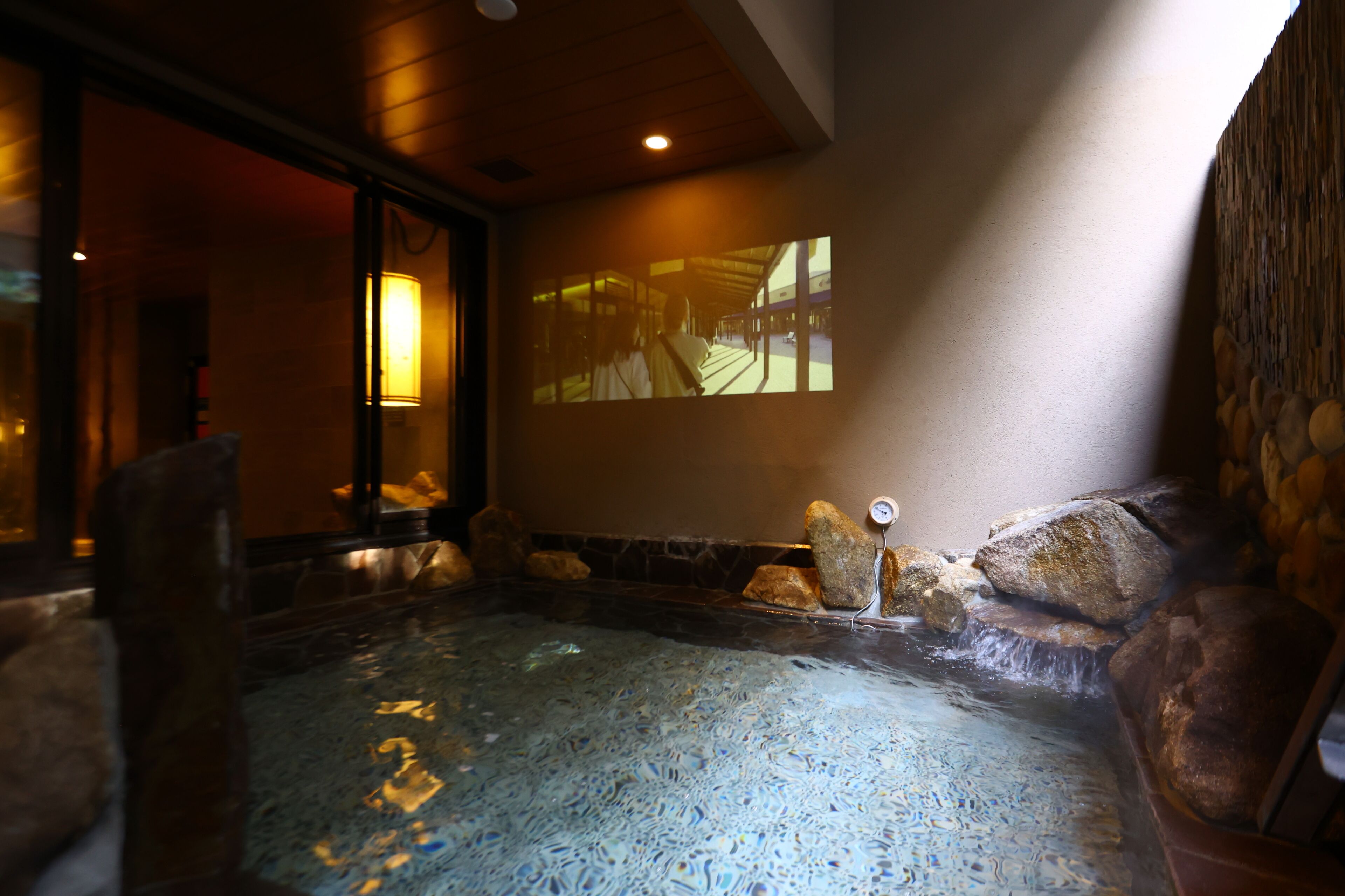 A spa area with a hot tub, stone walls, and a projection screen displaying a corridor scene.
