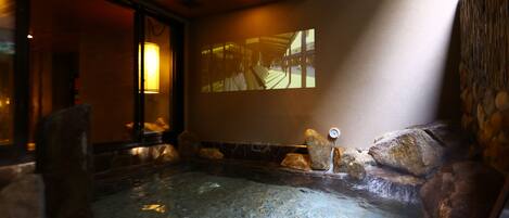 A spa area with a hot tub, stone walls, and a projection screen displaying a corridor scene.