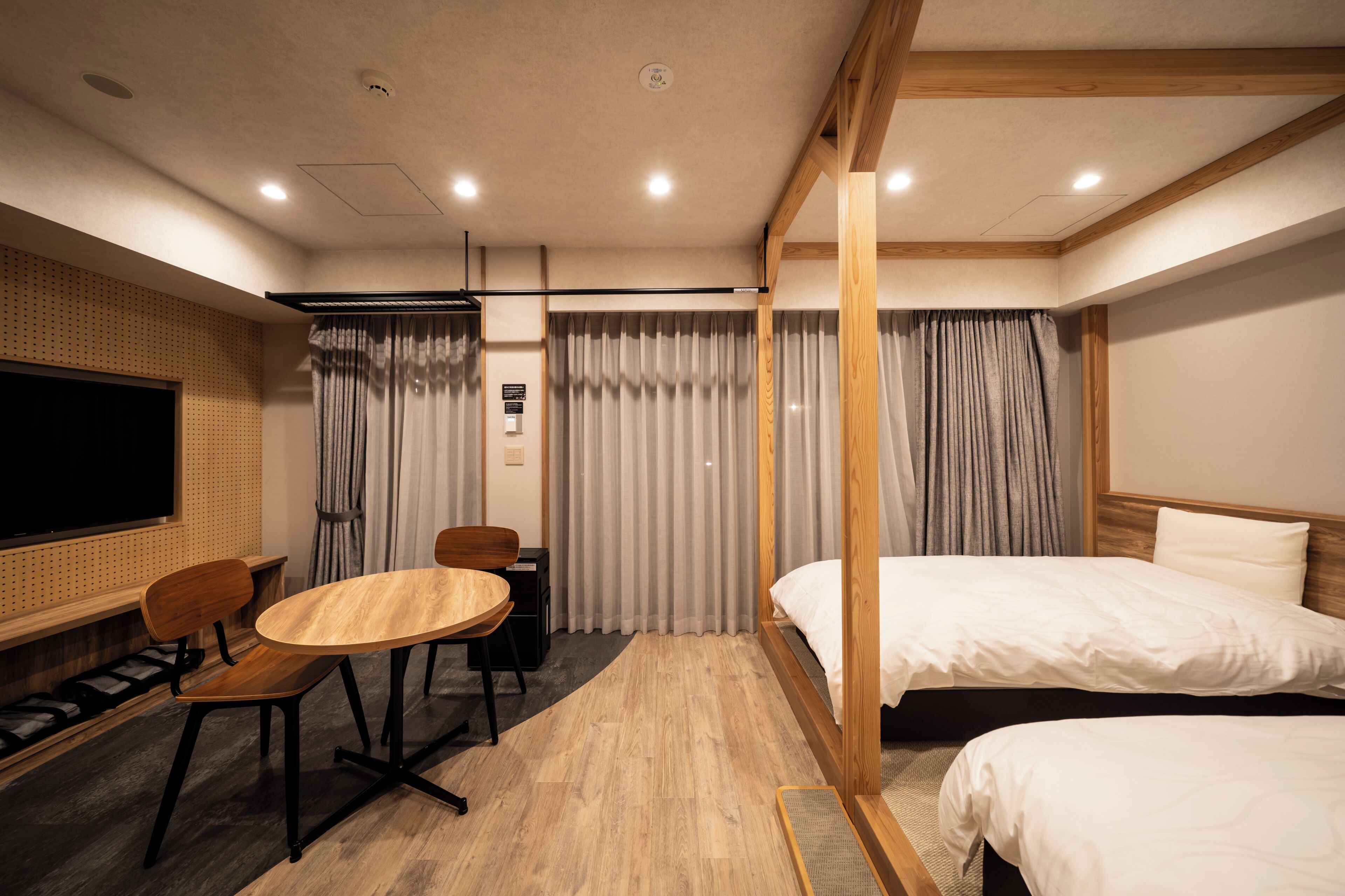 Une chambre d’hôtel avec un plancher en bois, un lit, un bureau avec une chaise, une télévision et des rideaux.