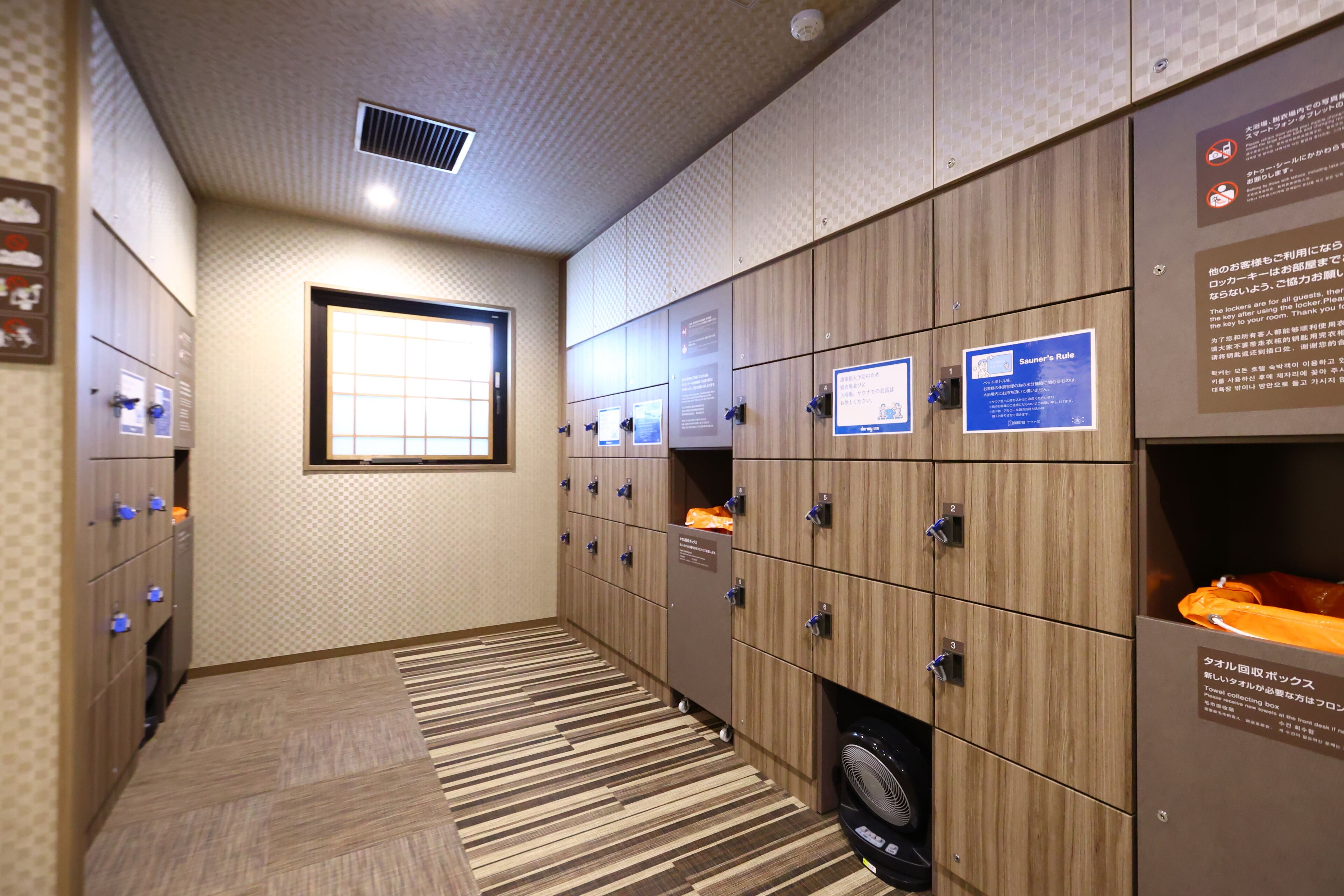 A hotel room with lockers, a window, and a fan.