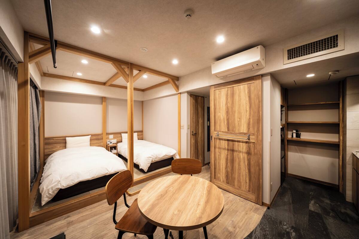 A hotel room with two beds, a wooden dining table, and a wardrobe.