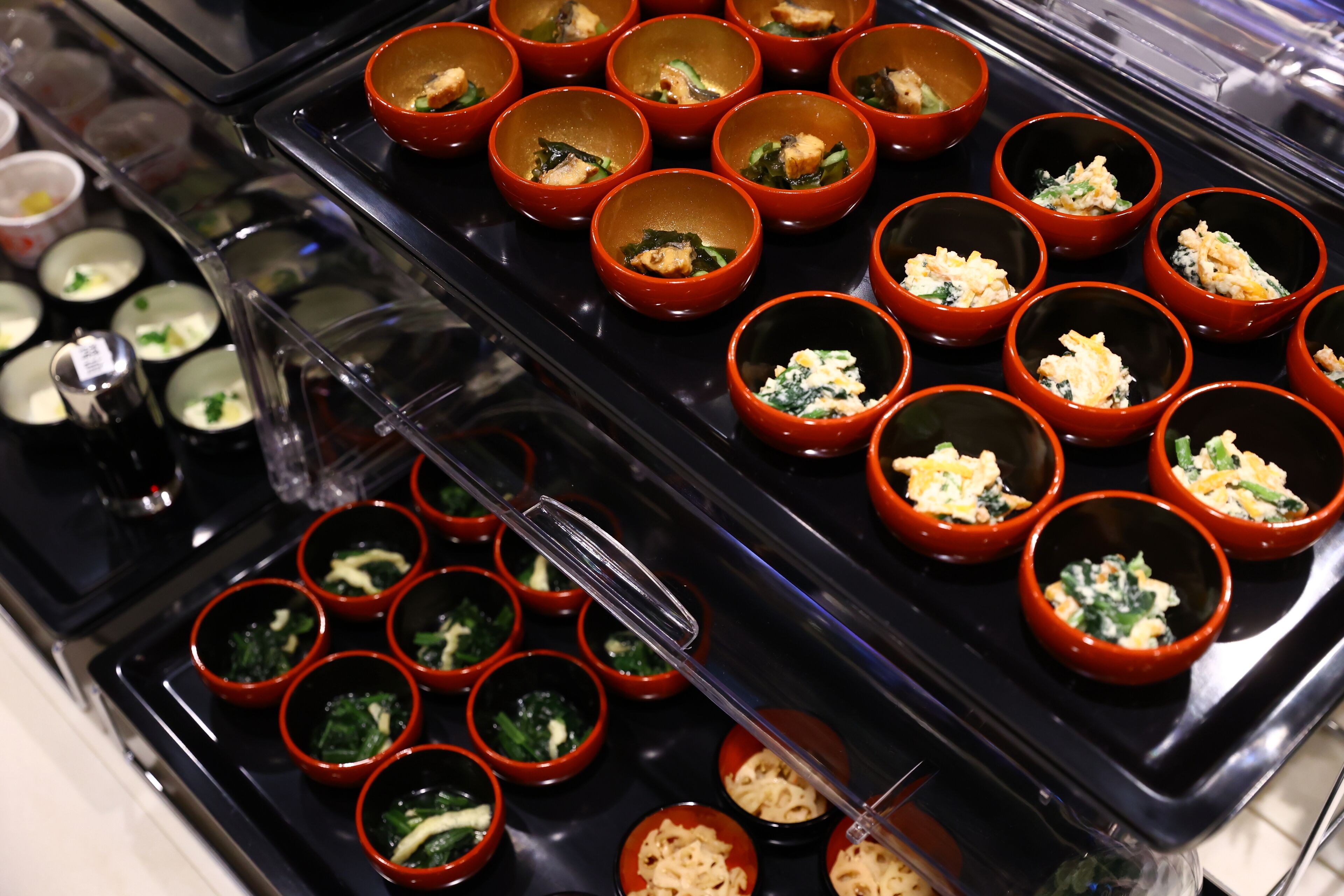 Een buffet met diverse gerechten, geserveerd in kleine schaaltjes en gerangschikt op een zwarte schaal.