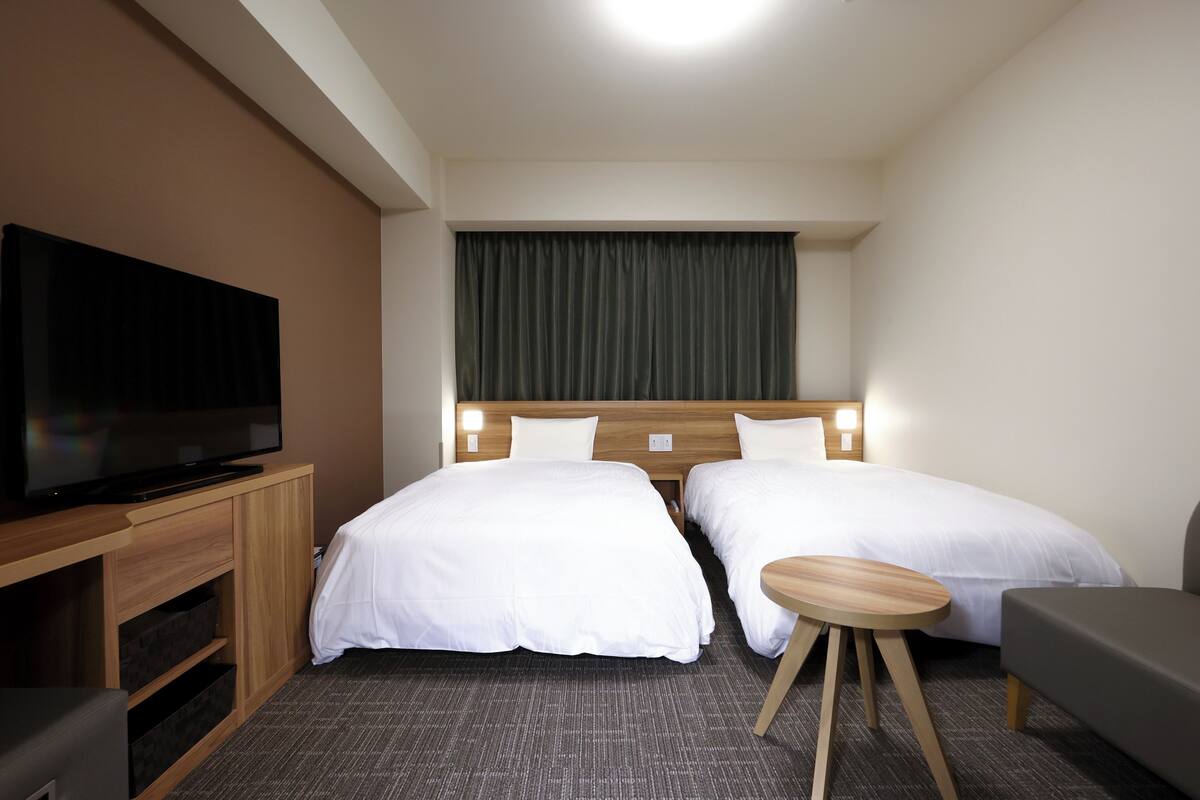 A hotel room with two beds, a TV, a small table, and a sofa.