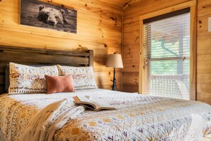 Une pièce de style cabane en bois, avec un lit, un livre, une lampe et un tableau représentant un ours accroché au mur.