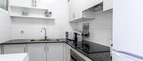 A compact kitchen with white cabinets, a granite countertop, a built-in oven, a microwave, and a sink.