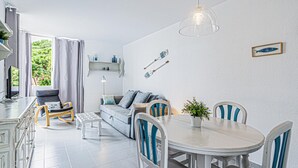 Een moderne woonkamer met een eethoek, een bank, een salontafel en een eettafel met stoelen. Er staat een televisie op een dressoir, een lamp en een plant op de tafel.