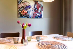 Une table à manger avec des sets de table, un vase rempli de fleurs et un tableau accroché au mur.