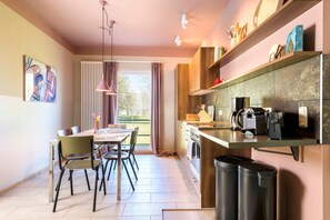 A modern kitchen with a dining area, featuring a large window, wooden cabinets, and a coffee machine.