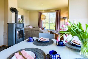 A dining area with a table set for two, a modern stove, and a view of the outdoors through large windows.
