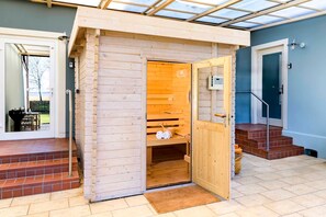 Eine Sauna mit Holzfassade, einer Tür und einem kleinen Ablagefach im Inneren.