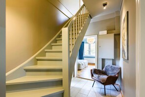 A staircase leading to a bedroom with a large window, a fluffy chair, and a bed.