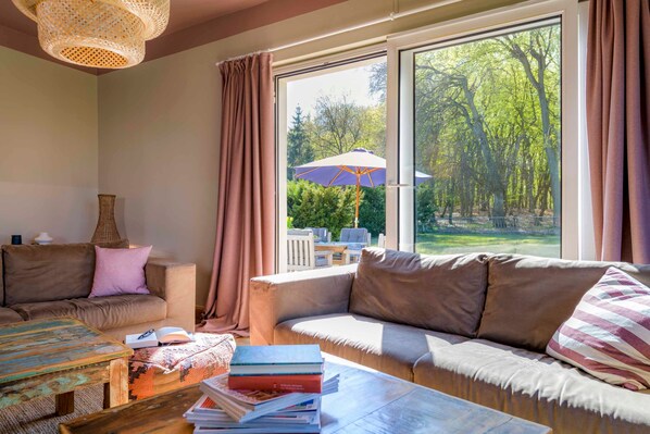 A cozy living room with a large window, a sofa, a coffee table, and a bookshelf.
