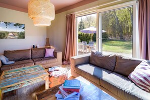 A cozy living room with a large window, a sofa, a coffee table, and a bookshelf.
