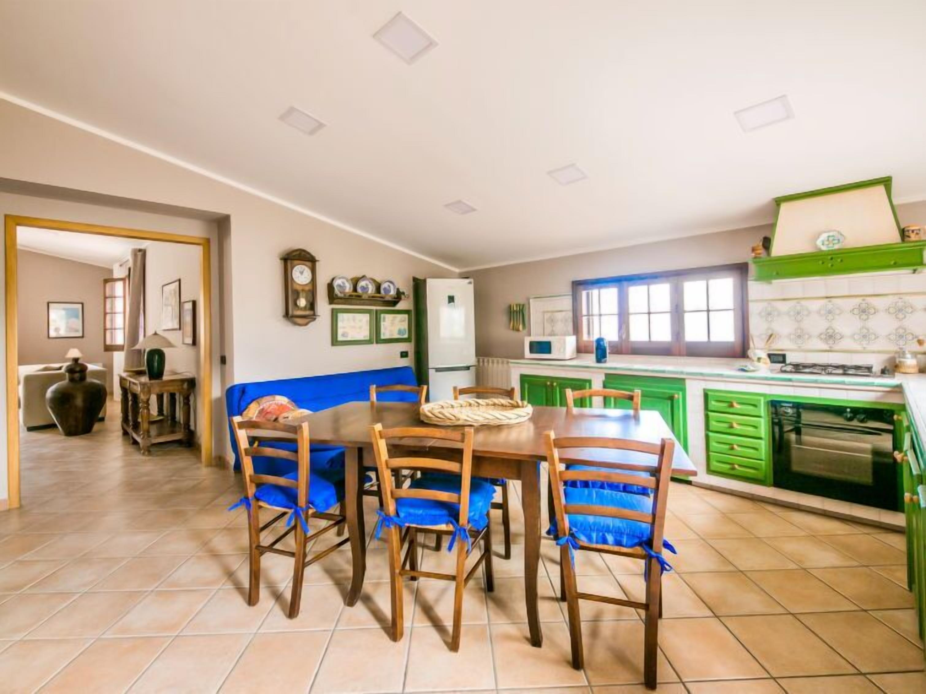 Un coin repas avec une table et des chaises en bois, une cuisine avec des meubles verts et une fenêtre donnant sur un beau paysage.