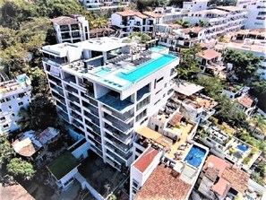 Un edifici d'alguns pisos amb una piscina al terrat, envoltat d'altres edificis residencials.