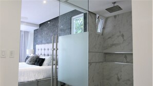Un dormitorio moderno con cabina de ducha de vidrio, paredes de mármol y una cama con cabecera capitonada.