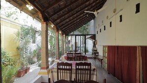 A covered dining area with tables and chairs, a ceiling fan, and a view of the outdoors. - Dumas Guest House (Puducherry)