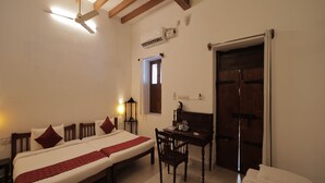 A hotel room with a large bed, a desk, a chair, a wardrobe, and a ceiling fan. - Dumas Guest House (Puducherry)