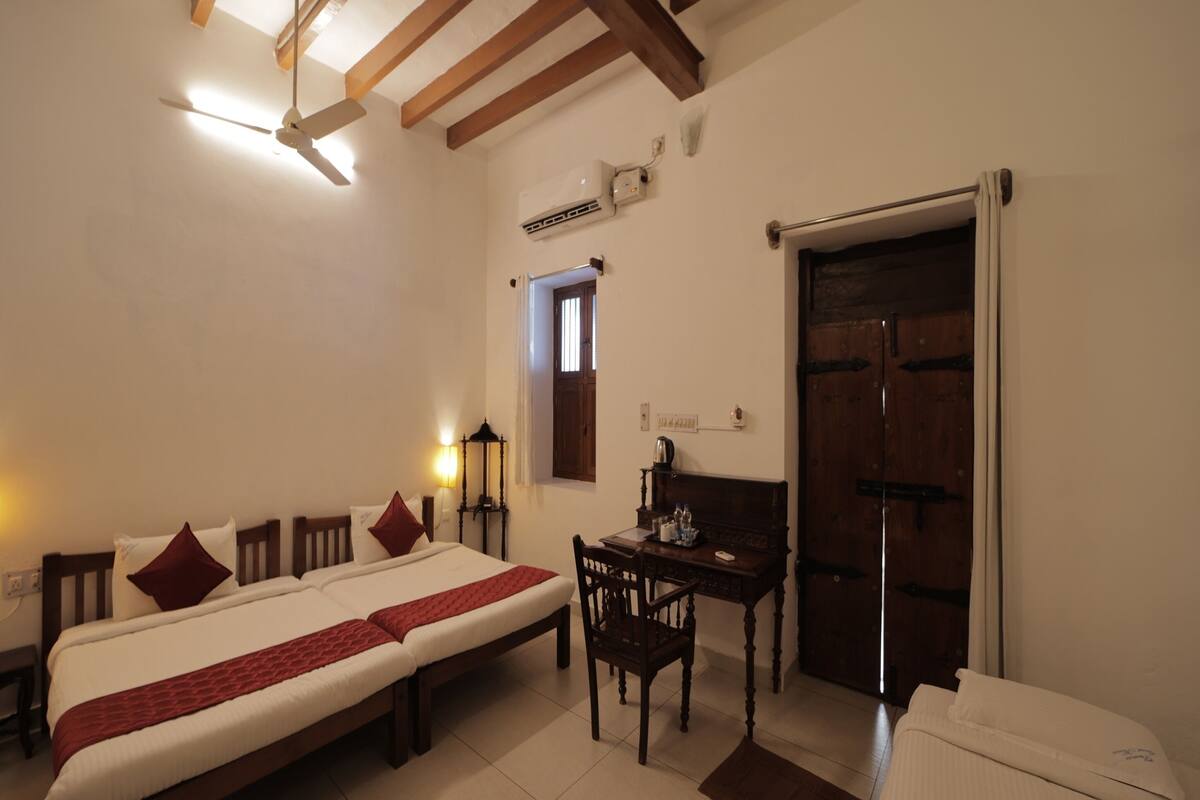 A hotel room with a large bed, a desk, a chair, a wardrobe, and a ceiling fan.