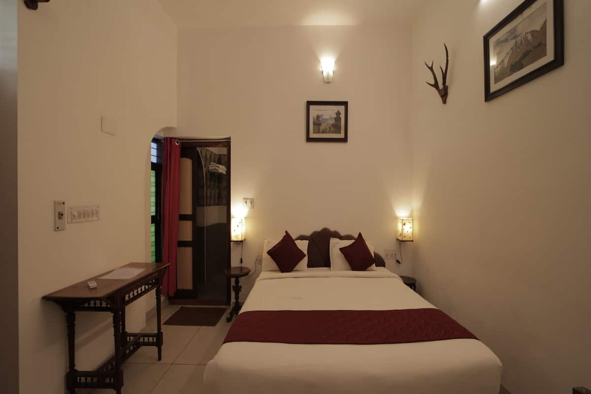 A hotel room with a large bed, bedside lamps, a wooden nightstand, a desk, and a shower area.