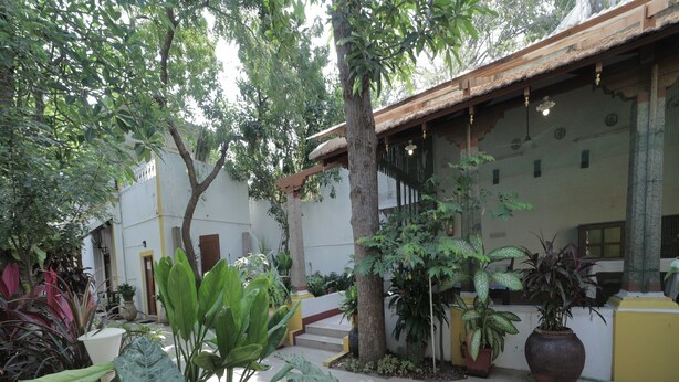 A courtyard with potted plants, a tiled floor, and a building with a tiled roof and windows. - Dumas Guest House (Puducherry)