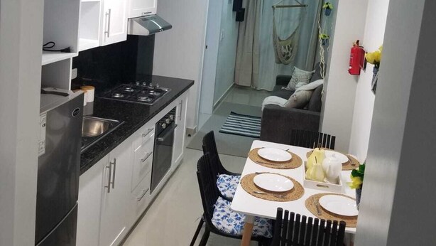A compact kitchen with white cabinets, a black countertop, and a dining area with a table set for two. - VAMAR LUXURY CONDO- MY PEACE APT (PUERTO PLATA)