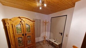 A room with a wooden cabinet with multiple doors, a small table with a bottle and papers, a chair, and a door. - Vacation apartment Untersberg up to 2 pers., 34 m², with terrace (Bischofswiesen)