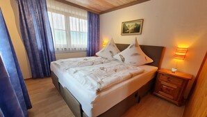 A bedroom with a bed, a nightstand, a lamp, a painting on the wall, and a window with curtains. - Vacation apartment Untersberg up to 2 pers., 34 m², with terrace (Bischofswiesen)
