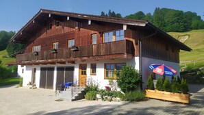 A two-story wooden building with a balcony, a sign advertising a restaurant, and a paved driveway. - Vacation apartment Untersberg up to 2 pers., 34 m², with terrace (Bischofswiesen)