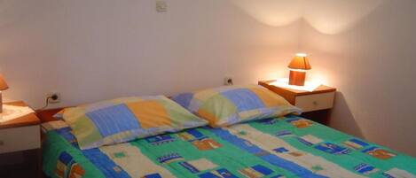 A single bed with a colorful quilt, a bedside table with a lamp, and a nightstand.