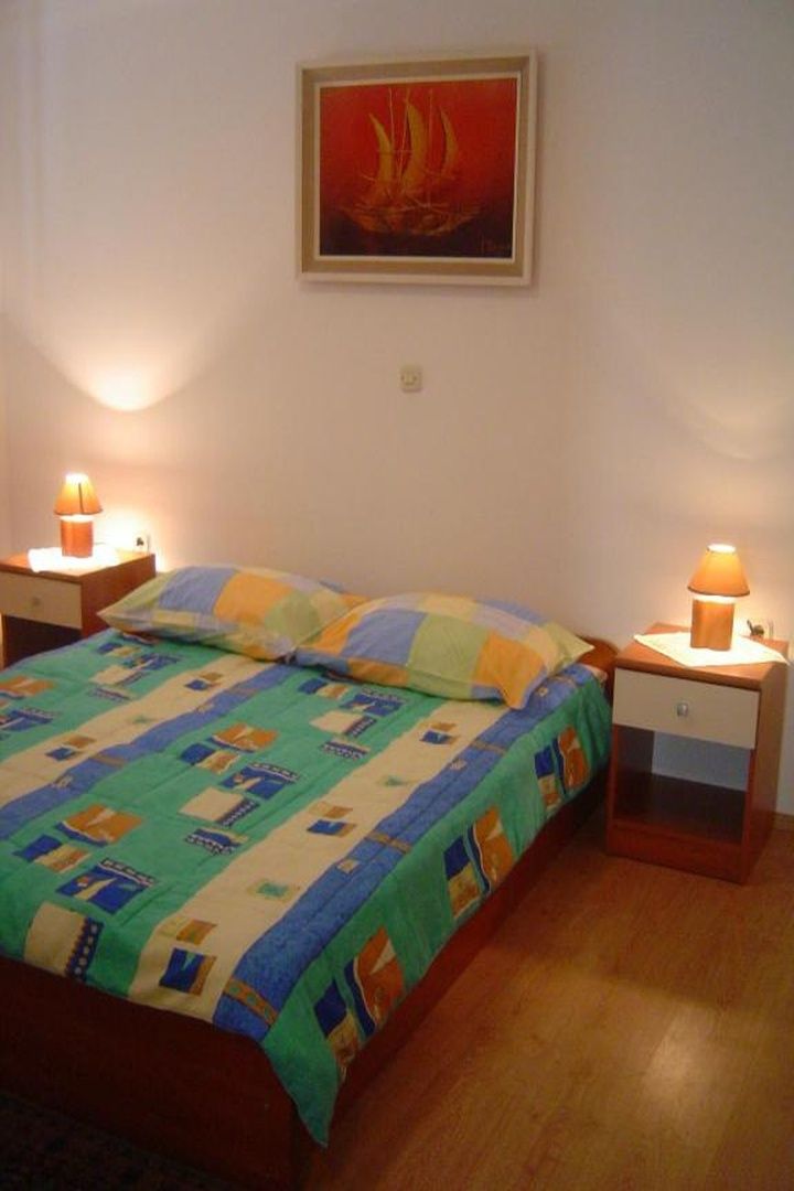 A bedroom with a bed, two bedside tables, a nightstand, a wall-mounted painting, and a lamp on each table.