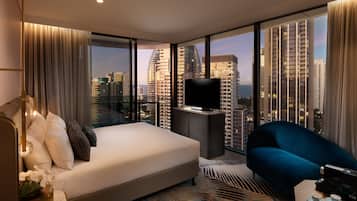A modern hotel room with a large bed, a sofa, a TV, and a city view.