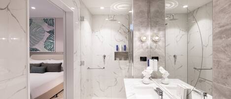 Un baño moderno con cabina de ducha de vidrio, tocador con azulejos de mármol y una cama con cabecero decorativo.