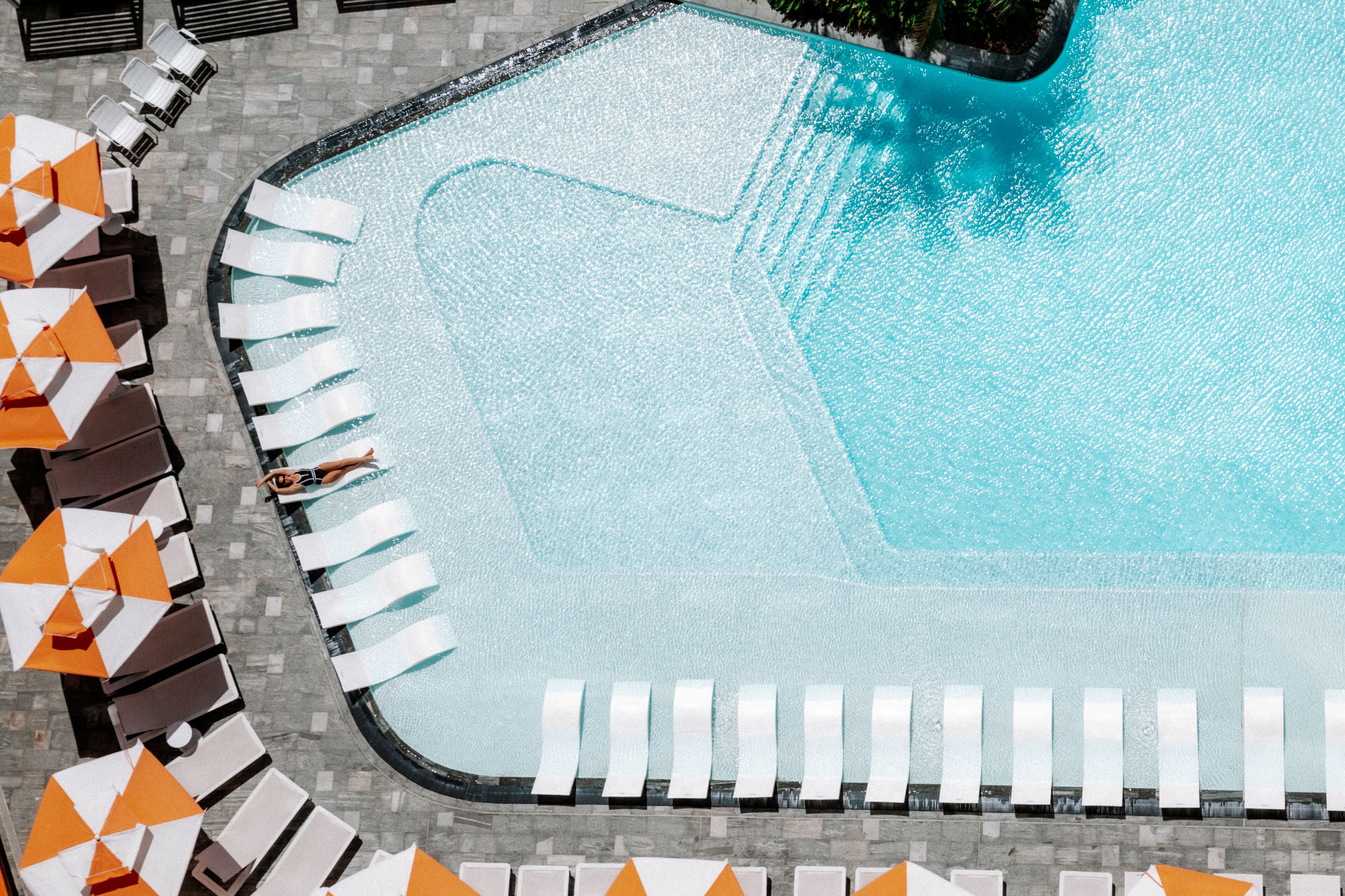 An aerial view of a swimming pool with lounge chairs and umbrellas arranged around it.