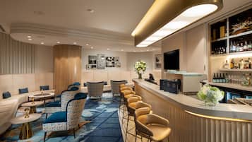 Un espace bar moderne doté d’un comptoir incurvé, de sièges avec des chaises à motifs, d’un téléviseur à écran plat et d’un présentoir à vins.