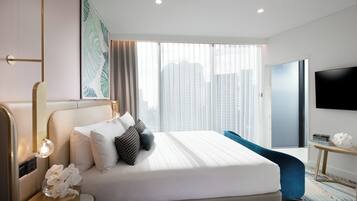 Habitación de hotel moderna con una cama grande, televisor, mesita de noche con lámpara y vista a la ciudad por la ventana.
