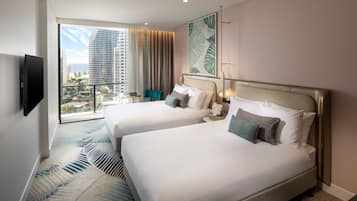 A hotel room with two beds, a large window with a city view, a flat-screen TV, and a patterned carpet.